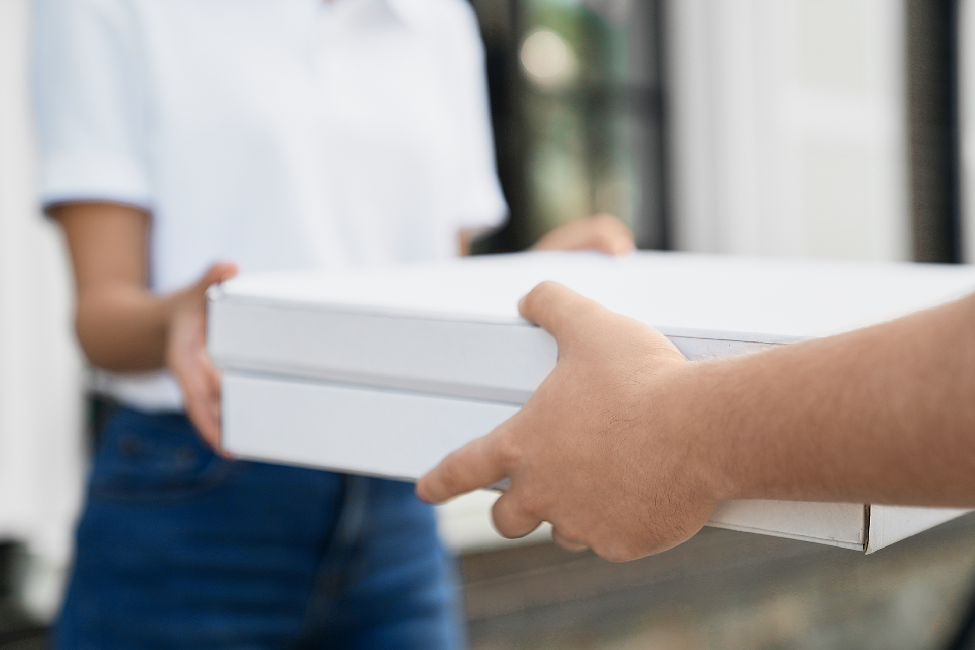 Selective focus of male hands giving two boxes of pizza to woman. Close up of incognito female in casual outfit receiving order from deliveryman outdoors. Food delivery concept.